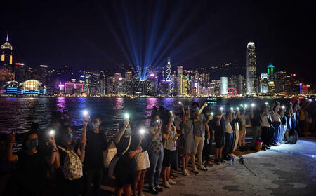 a line of people holding hands against a victoria harbour night