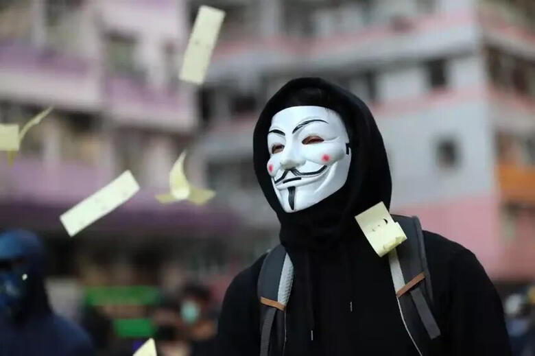 a joss paper floats around a protester wearing a guy fawkes mask