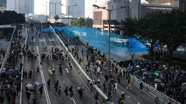 protesters running away from a water cannon truck on a road